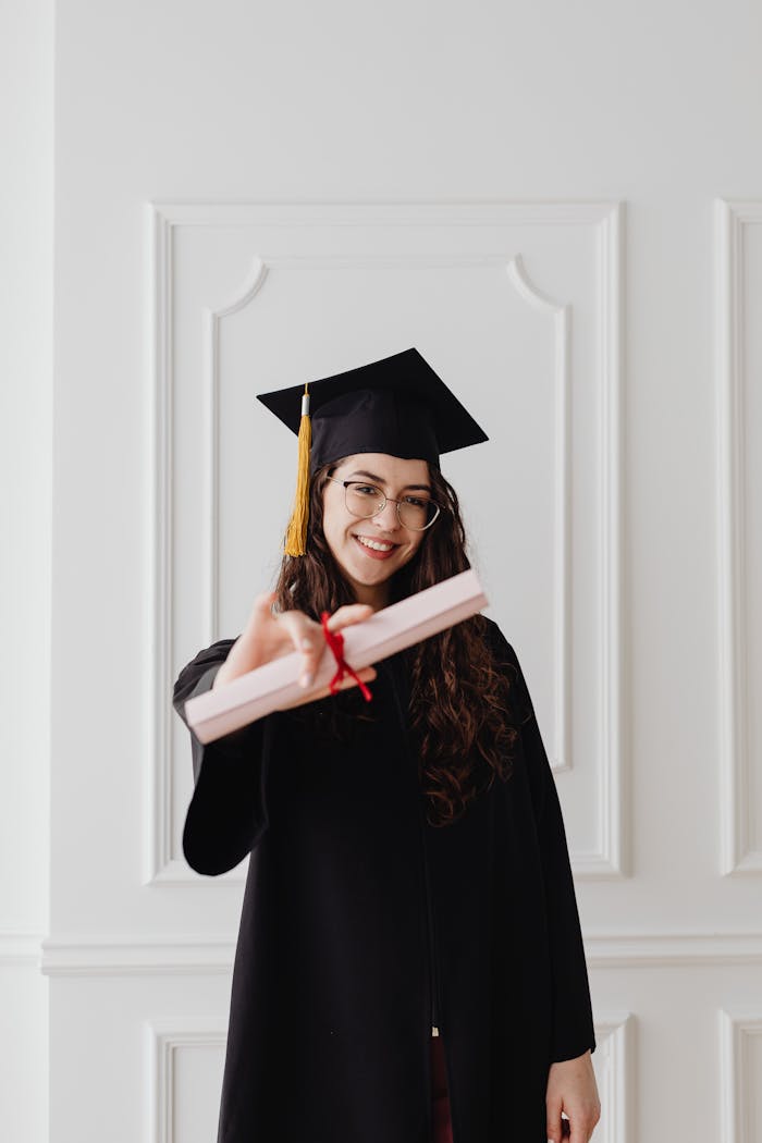 Young woman in graduation attire, smiling proudly with her diploma against a classic backdrop.